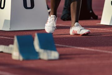 An athlete wearing white shoes waits at the starting line.