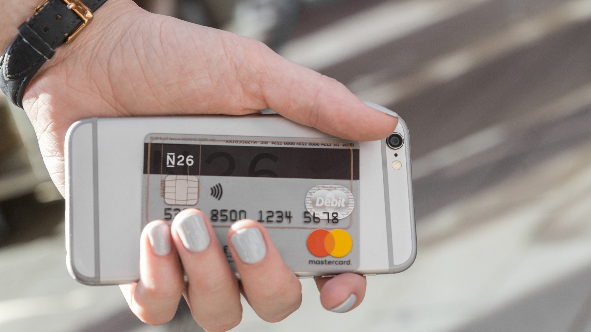 N26 Pressefoto einer Hand, welche ein Smartphone hält. Vor dem Smartphone hält sie eine durchsichtige N26 Mastercard.