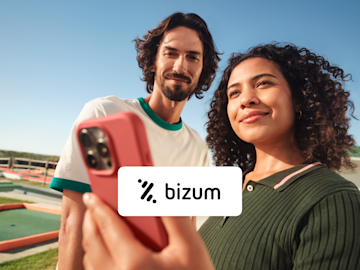 A couple stands outdoors looking at a smartphone, with a card displaying the Bizum logo overlaid.
