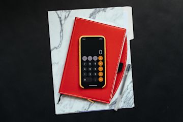 A smartphone set on calculator on top of notebooks.