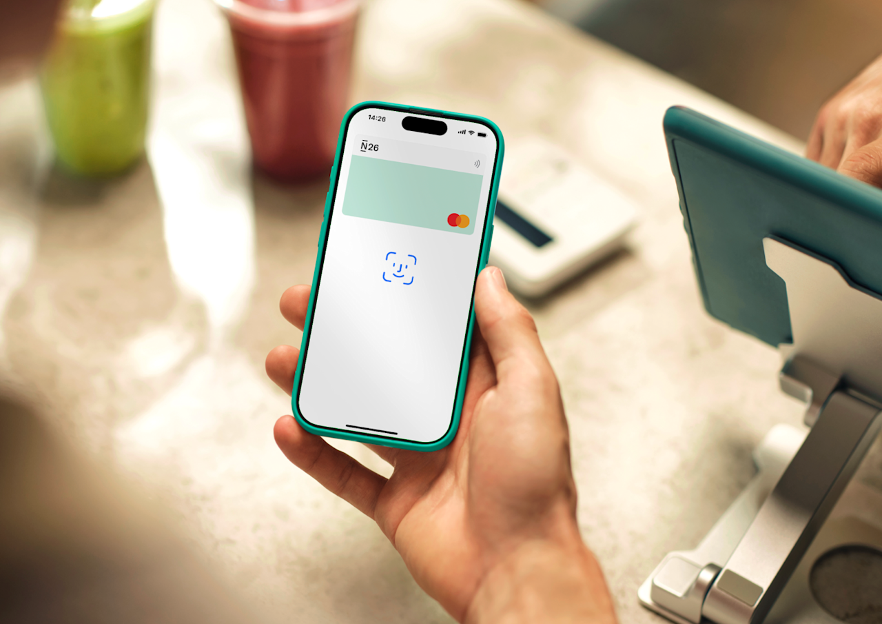 Une main tient un smartphone affichant l'invite Face ID pour un paiement sans contact sur un comptoir.