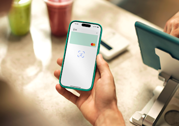 A hand holds a smartphone displaying the Face ID prompt for a contactless payment at a counter.