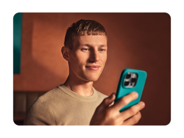 A man smiles while looking at the screen of his smartphone with a teal-colored case.