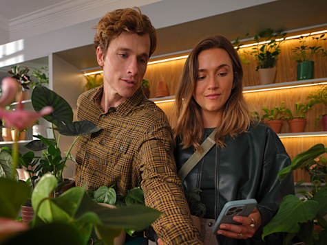 Un hombre y una mujer miran un smartphone mientras están rodeados de muchas plantas en macetas en una tienda.