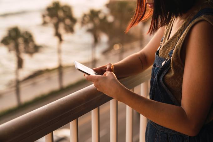 Une femme utilise son smartphone sur un balcon.