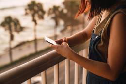 Junge Frau schreibt eine Textnachricht auf einem Balkon.