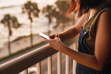 Girl texting on a balcony with a breach in the background.