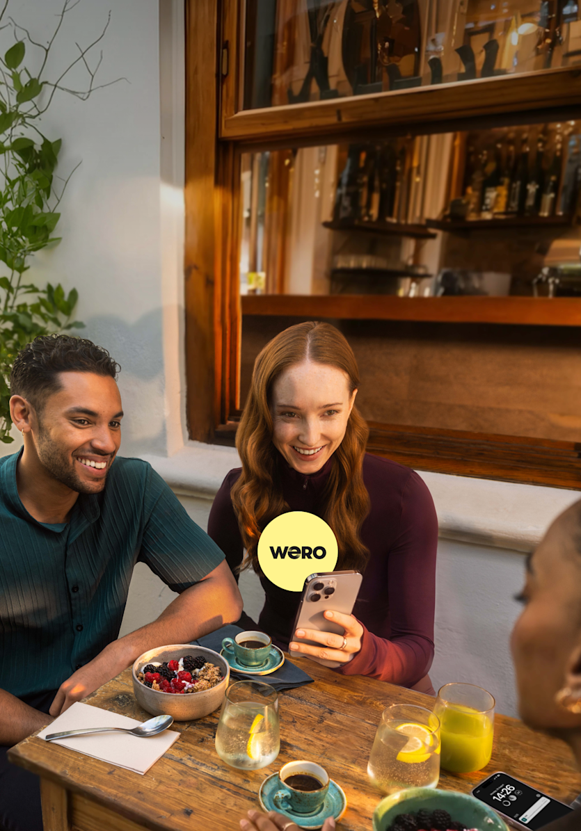 A man and a woman holding her phone in a restaurant talking to a friend with a WERO icon.