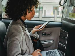 Une femme travaille dans une voiture avec son ordinateur portable et son smartphone.