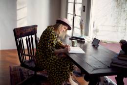 Eine Frau sitzt auf einem Schreibtisch und schreibt in ein Notizbuch.