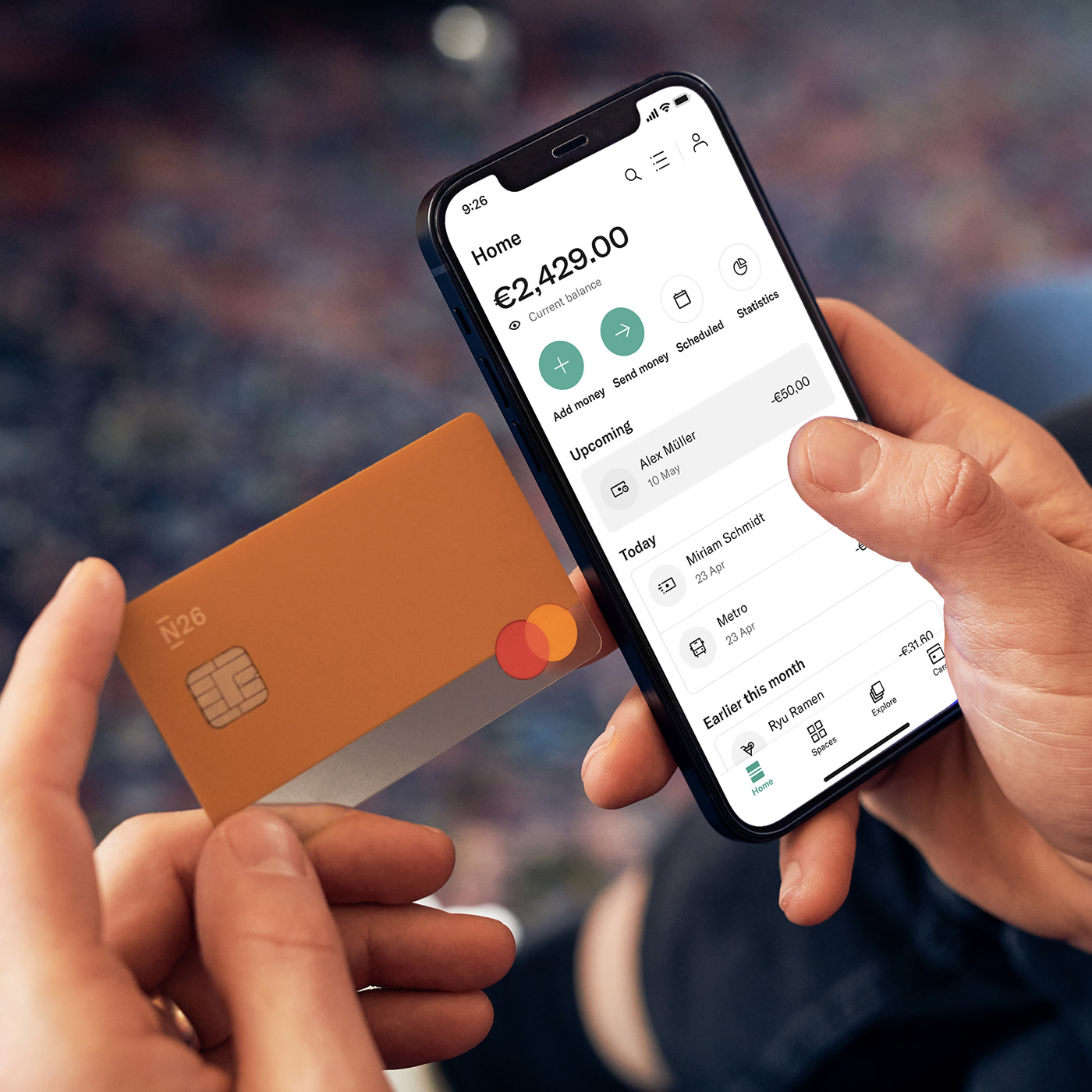 Image showing a person with an N26 debit card and the N26 app displaying the account feed with the list of transactions.