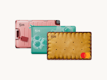 Tre Mastercard N26 fantasiose sono impilate, stilizzate come una valigia rosa, una saponetta e un biscotto.