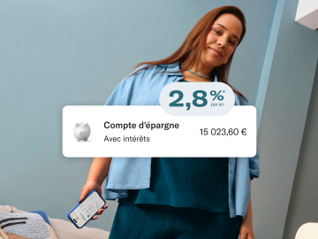 Femme vêtue de bleu, assise et tenant son téléphone portable avec l'application N26 ouverte. Au premier plan, image du taux de 2,8% p.a. taux d'intérêt, solde du compte principal et du compte d'épargne.