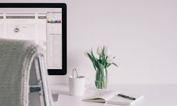 Freelance desk with computer, plants, notes, cup.