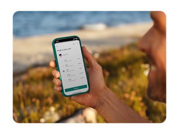 Una persona tiene in mano uno smartphone che mostra le opzioni dei piani dati per gli Stati Uniti, con quantità di GB e prezzi variabili, su uno sfondo esterno sfocato.