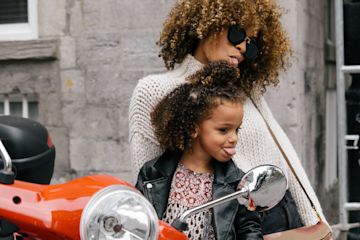 Mother and daughter look in scooter rearview mirror.