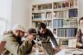 A group of three MBA students point to a laptop in a library while laughing.