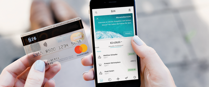 A person holding an N26 Mastercard and a smartphone with the N26 app open.