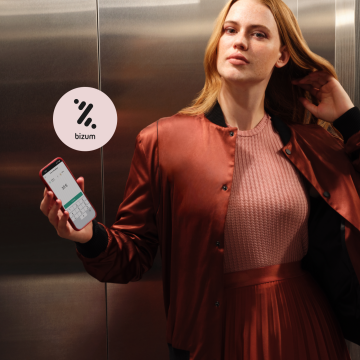 Mujer con un vestido rojo sosteniendo un mobile con la app de N26 y en el fondo el logo de Bizum. 