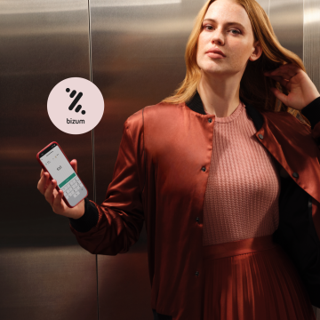 Woman in a red dress holding a mobile phone with the N26 app and the Bizum logo in the background.