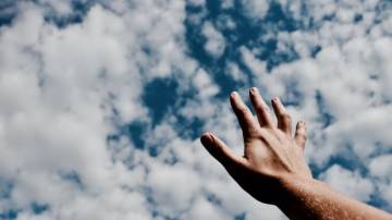 Hand reaching to the sky and clouds.
