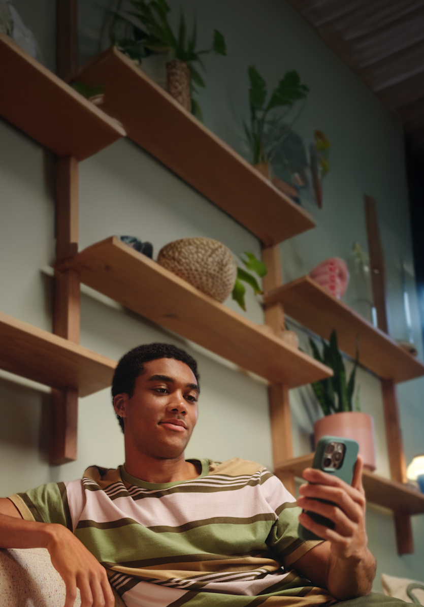 Un joven está sentado en un sofá mirando la pantalla de su smartphone en casa.