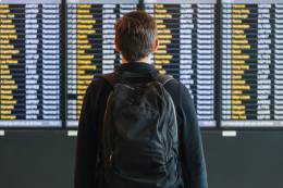 Giovane con uno zaino che controlla l'orario dei voli all'aeroporto.