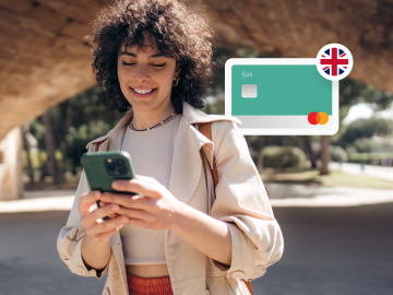 imagen de una mujer joven parada en un parque y mirando su teléfono, con una tarjeta n26 y una bandera británica al fondo.