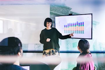 A person standing next to a TV in a meeting room giving a presentation.
