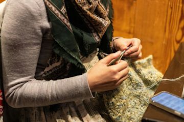 Una persona con una sciarpa, che sta lavorando a maglia.