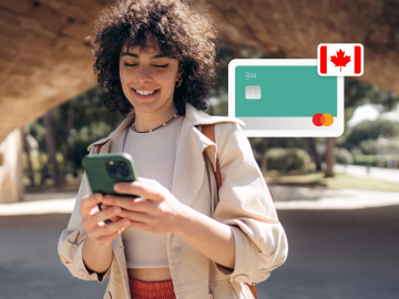 imagen de una mujer joven parada en un parque y mirando su teléfono, con una tarjeta n26 y una bandera canadiense al fondo.