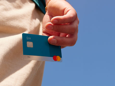 A hand holding a petrol N26 card against a backdrop of clear blue sky.