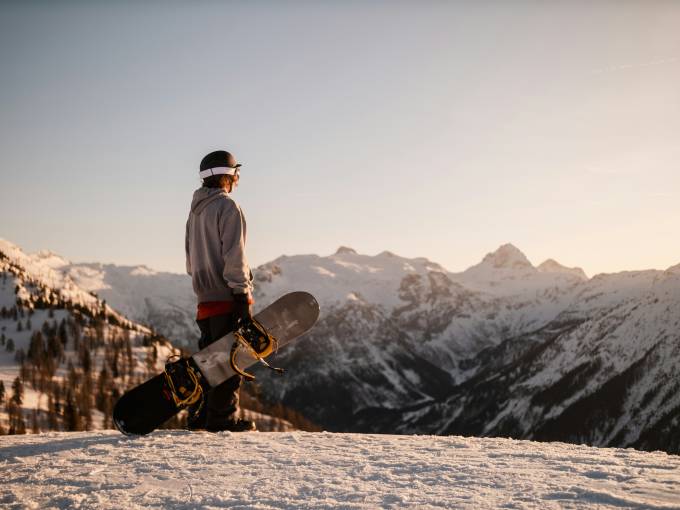 Uno snowboarder su una montagna guarda verso l'orizzonte.