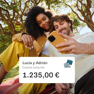 Maya y Marco sentados en un parque. Maya sostiene su tarjeta N26 y Marco mira su móvil. En primer plano aparece una ventana emergente con la cantidad de dinero en su cuenta conjunta.