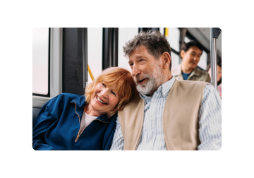 A couple sitting on a bus, the woman leaning on the man's shoulder and smiling.