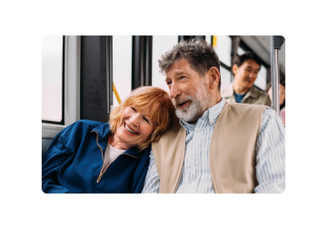 Una coppia siede insieme su un autobus, la donna si appoggia alla spalla dell'uomo e sorride.