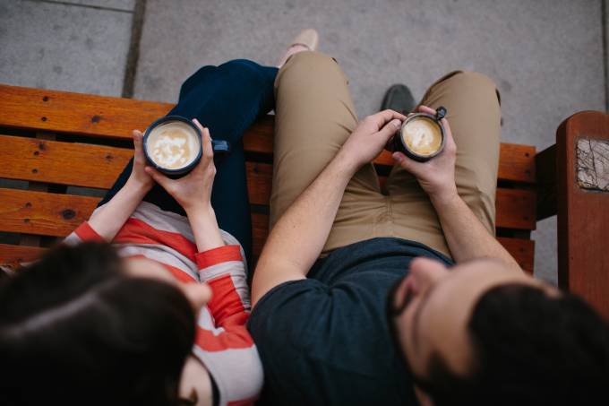 Man and a woman sitting on a bench and drinking coffee.