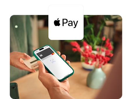 Eine Person hält ein türkisfarbenes Smartphone über ein Kartenterminal, um eine kontaktlose Zahlung mit Apple Pay und einer virtuellen N26-Karte zu tätigen.