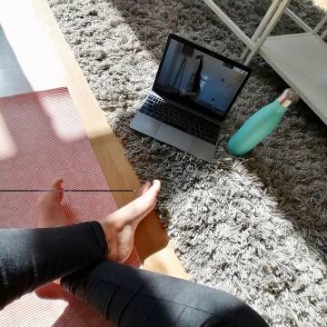 Laptop, water bottle and person wearing leggings sitting on the carpet.