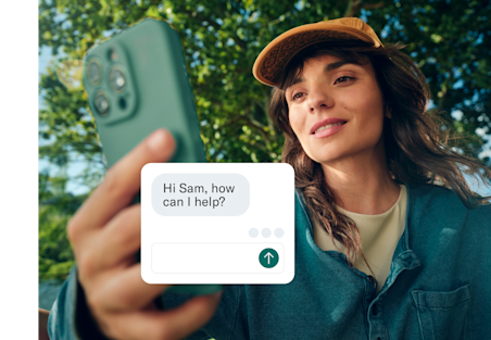 A woman holds her phone toward the camera, with a customer service chat box overlaid on the screen.