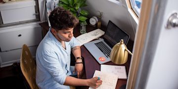 A man writing down his idea on a white book on a small wooden table.