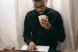 A guy using a laptop and drinking coffee.