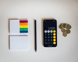 Smartphone con algunas monedas y un lápiz con papeles colocados de forma ordenada sobre un fondo blanco.
