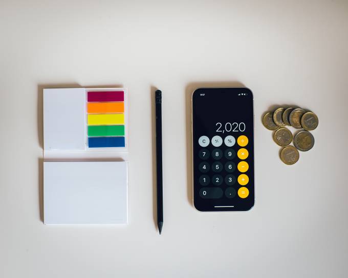 Smartphone con algunas monedas y un lápiz con papeles colocados de forma ordenada sobre un fondo blanco.