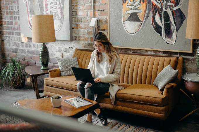 Woman works on a laptop on her sofa. 