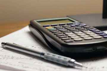 una calcolatrice e una penna appogiati su un quaderno.