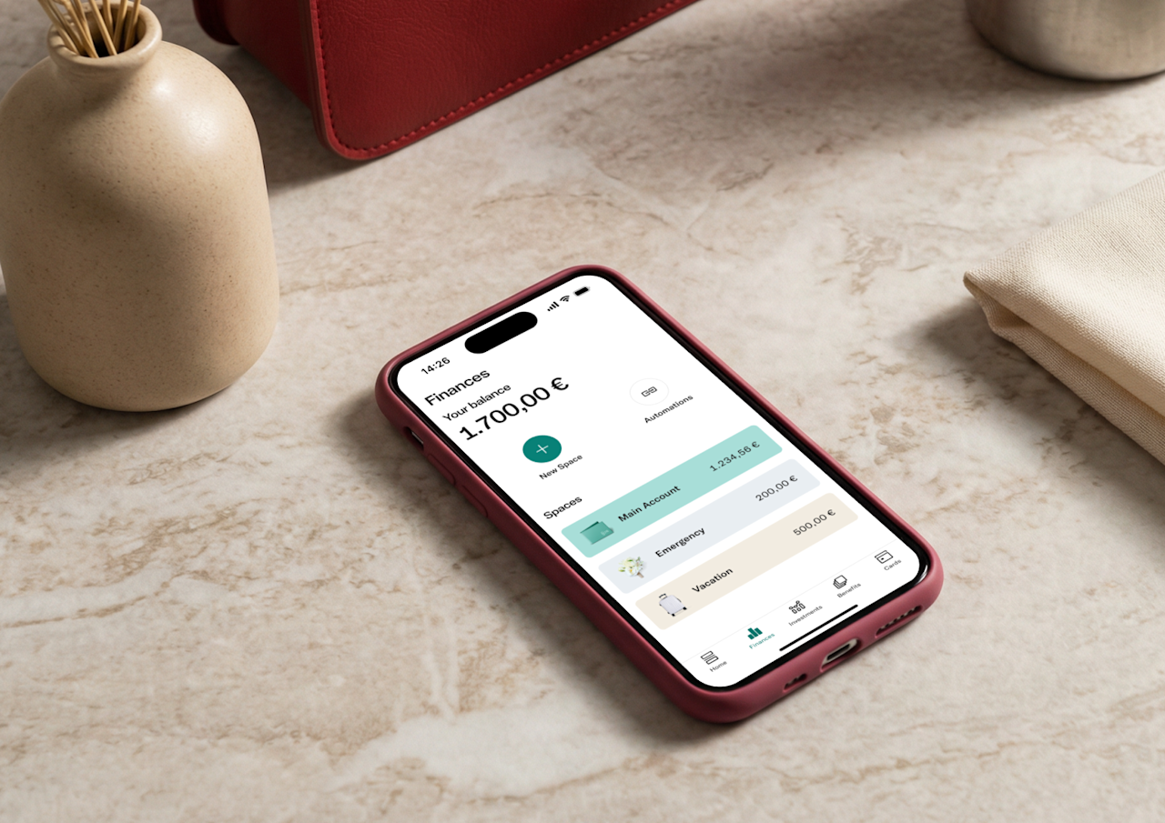 A pink smartphone on a marble surface displays the N26 app finances screen with a balance of 1.700,00 € and categorized sub-accounts for emergency and vacation funds.