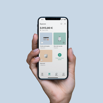 Una mano che tiene in mano un iPhone X con lo schermo degli Spazi aperto sull'app N26.