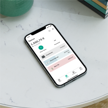 A hand holding an iPhone X in their hand with the Spaces screen open on the N26 app.