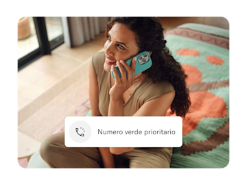 Una donna sorridente è seduta in casa e parla al telefono, con un'icona "Priority hotline" sovrapposta all'immagine.
